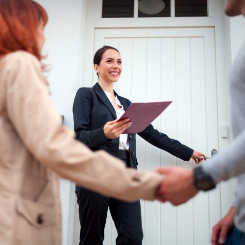 Real estate agent near door inviting young couple to enter house Real estate agent near door inviting young couple to enter house for visit