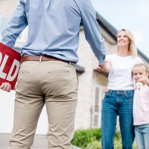 cropped shot of realtor with sold sign shaking hand of young woman with daughter in front of new house